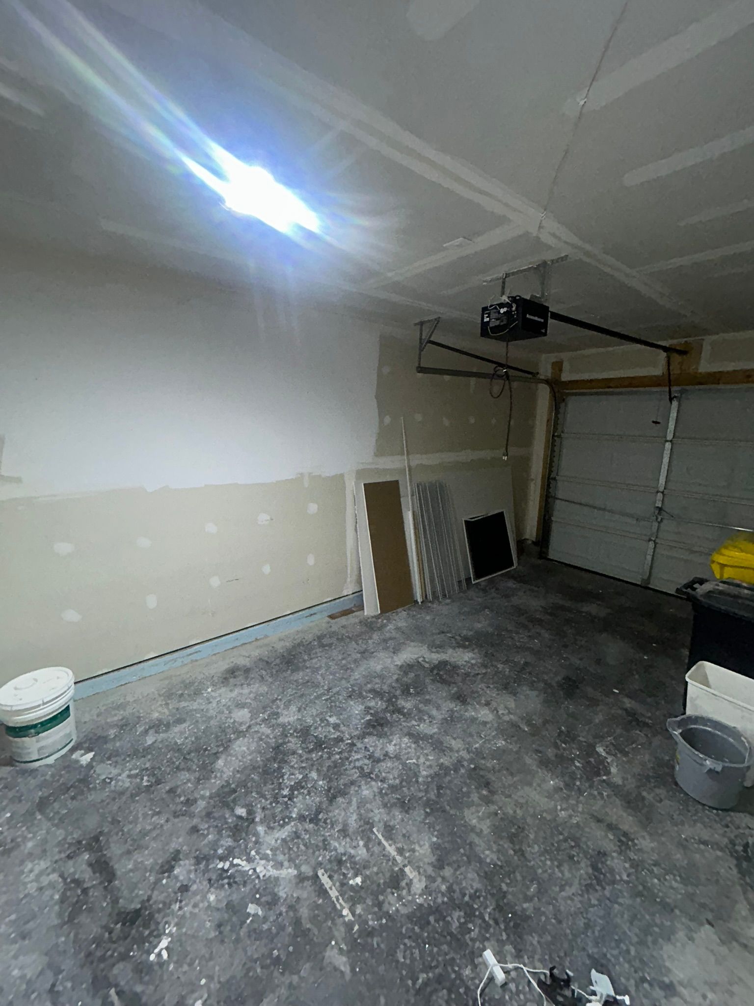 Empty garage with unfinished drywall, concrete floor, and garage door under bright ceiling light.