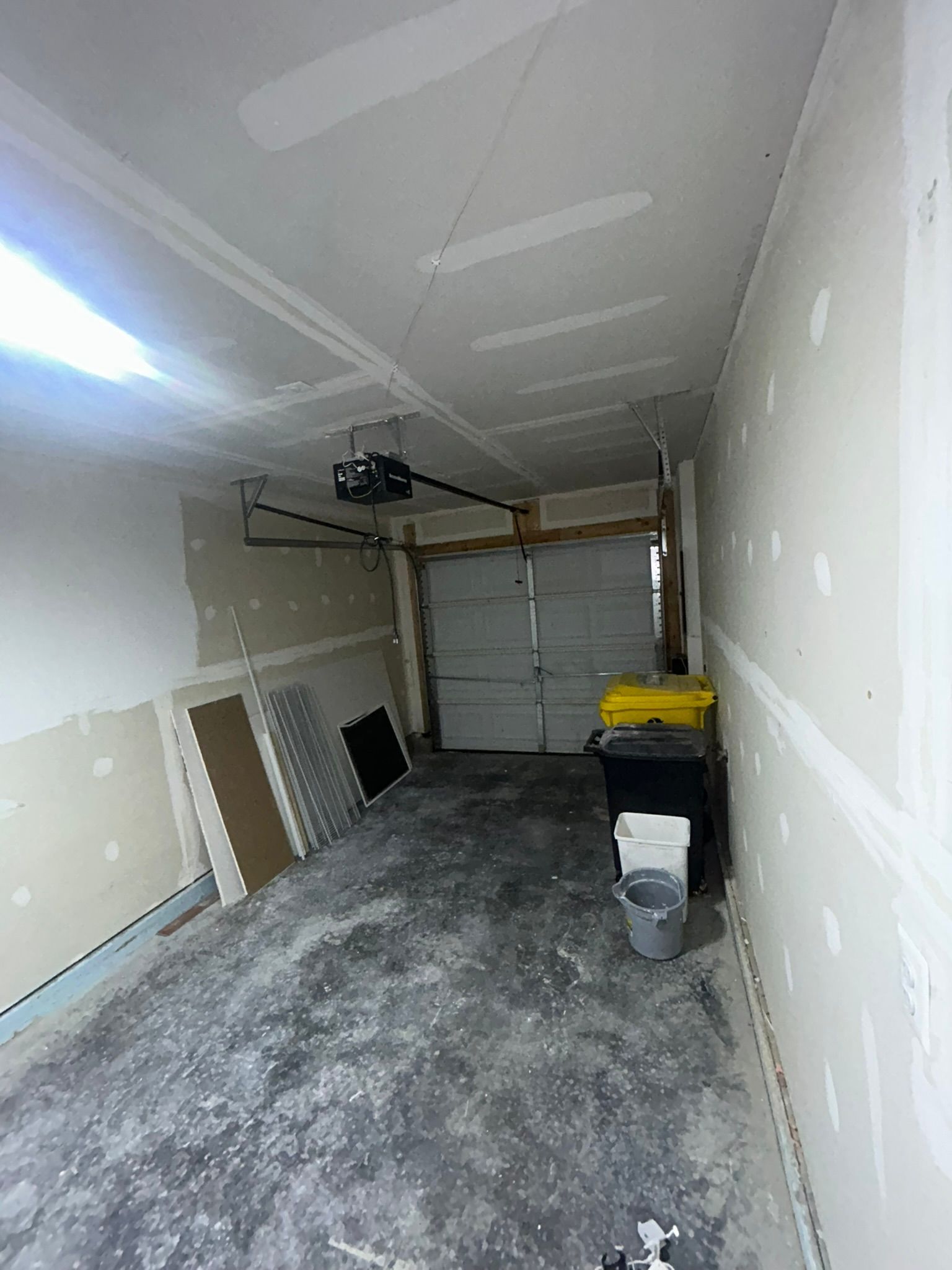 Empty single-car garage with concrete floor, white walls, and stored items along the right side.