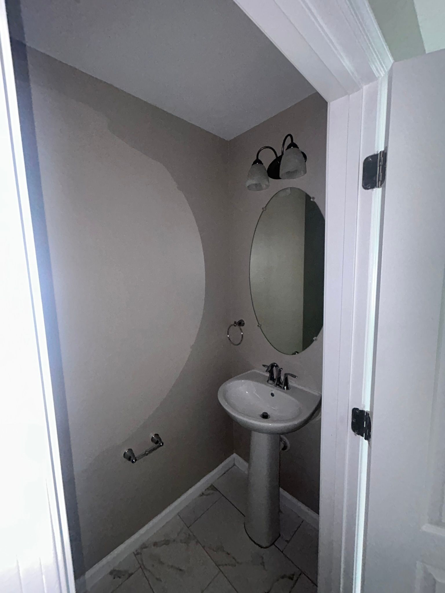 Small narrow bathroom with a pedestal sink, oval mirror, gray walls, and tiled floor.