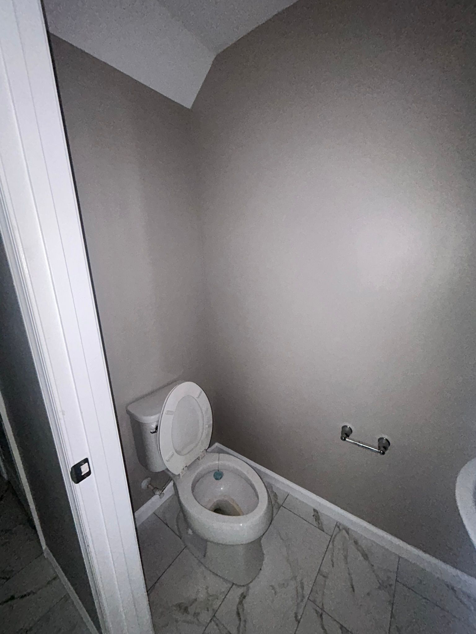 Small gray bathroom with a toilet and marble-patterned floor, seen from the doorway.