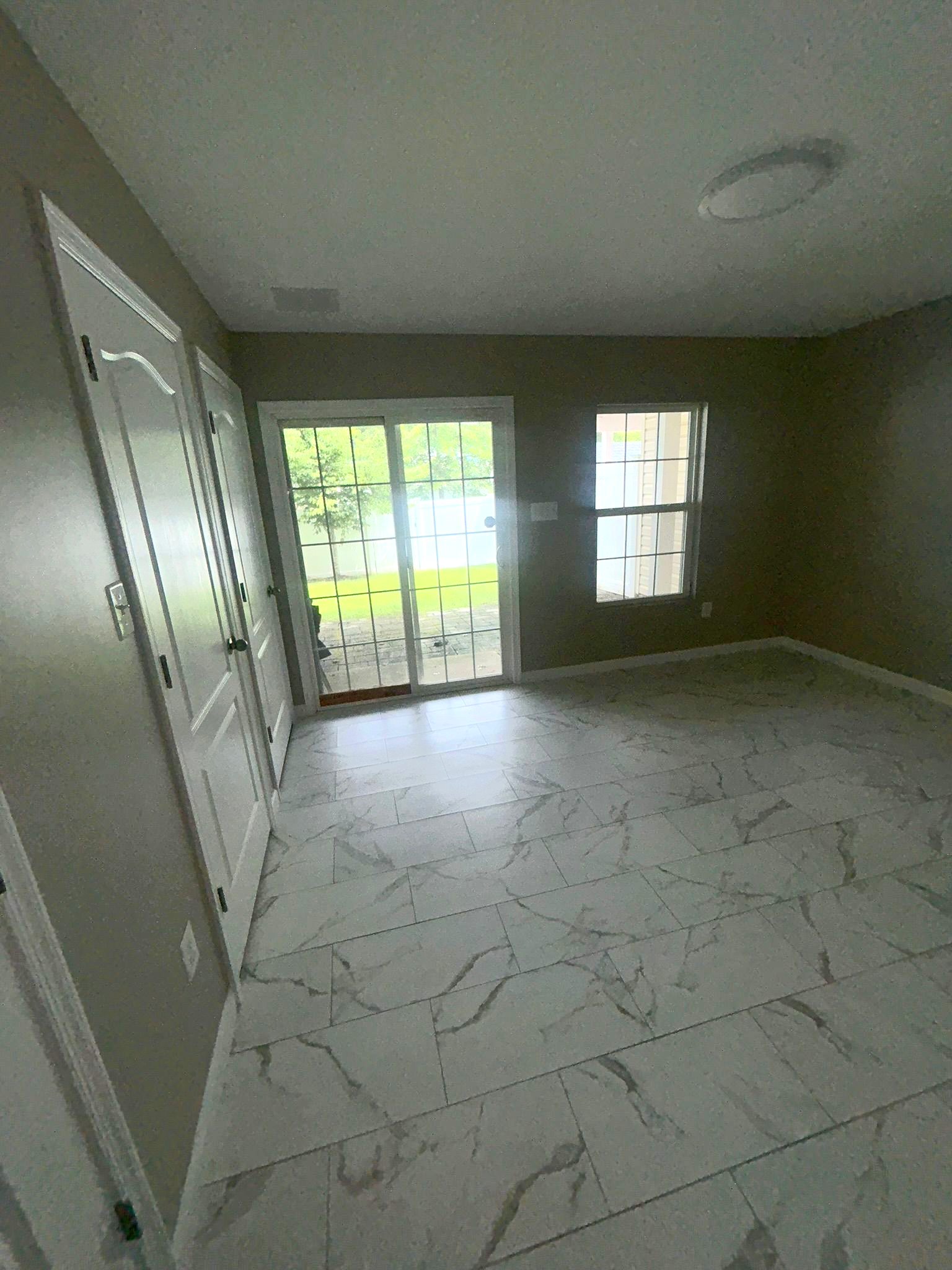 Empty room with white tiled floor, gray walls, and bright French doors leading outside.