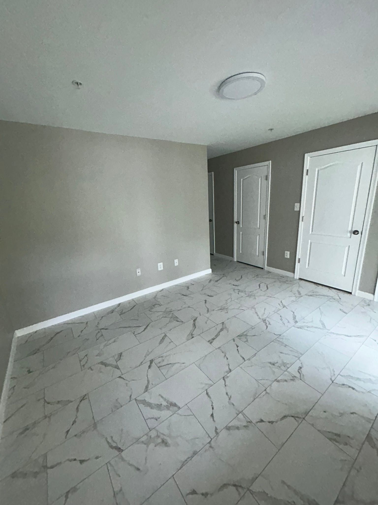 Empty gray bedroom with white tiled floor, closet doors, and a ceiling light fixture.