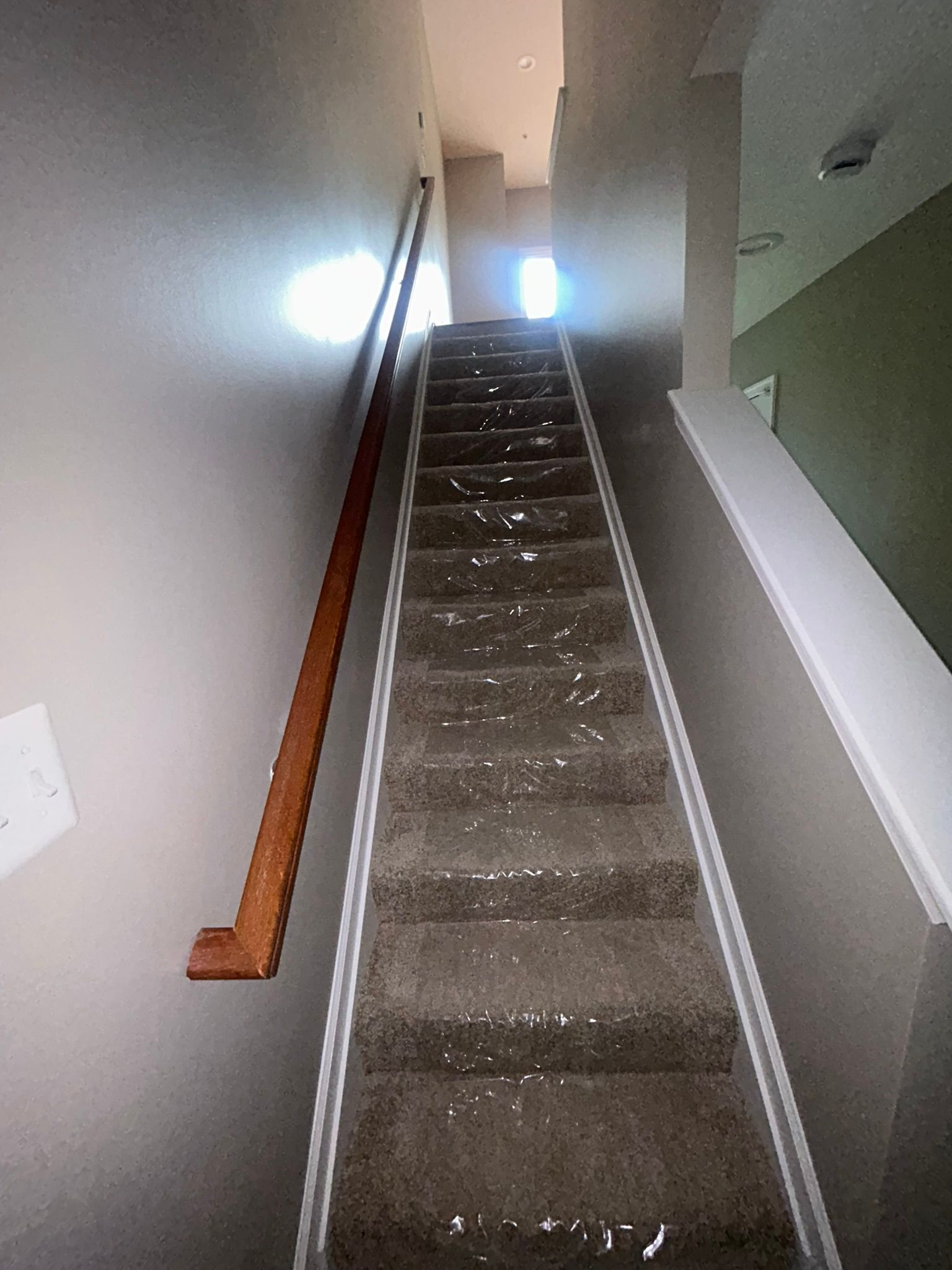 Narrow indoor staircase with carpeted steps, white walls, and a bright window at the top.