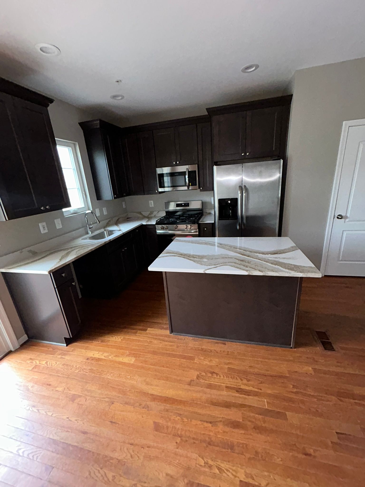Modern kitchen with dark cabinets, stainless steel appliances, and a large island on hardwood floors