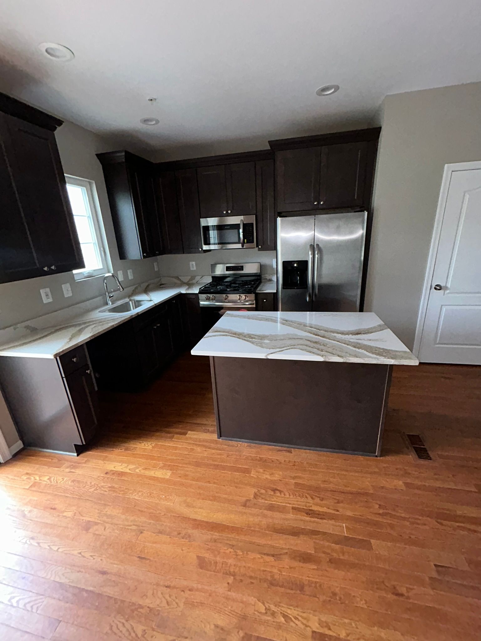 Modern kitchen with dark cabinets, stainless fridge, island, and hardwood floors