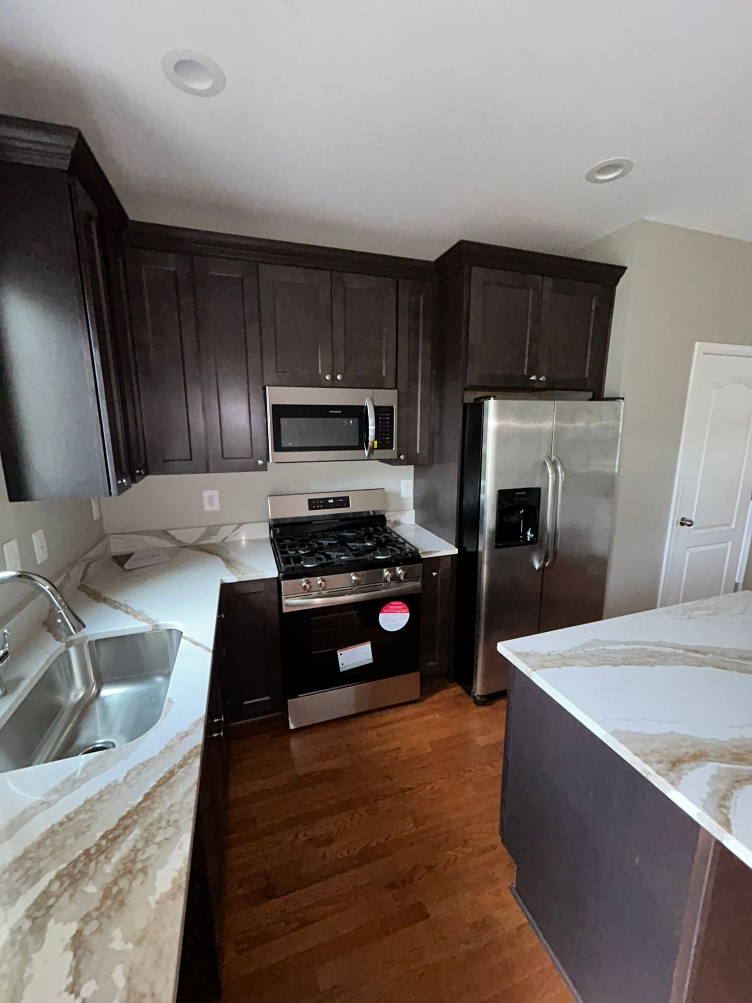 Modern kitchen with dark cabinets, stainless appliances, wood floor, and white countertops