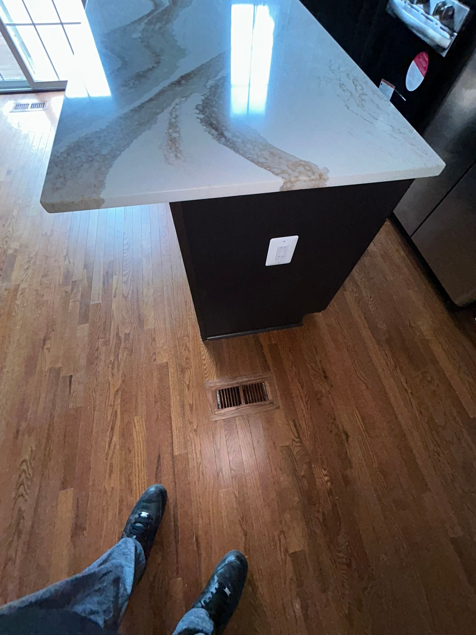 Kitchen island with white marble countertop and wood floor, viewed from above with someone’s shoes visible nearby