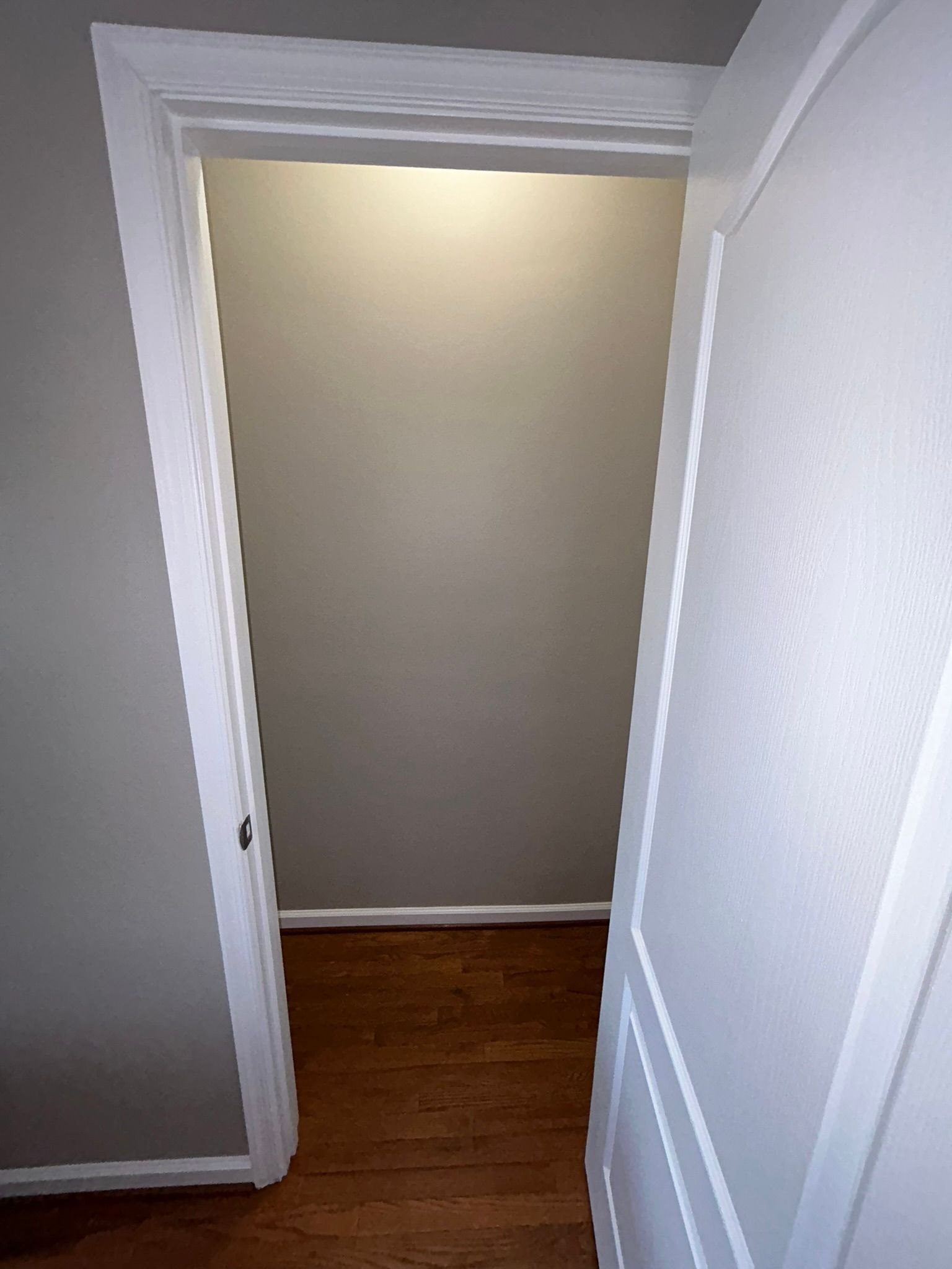 Open white doorway leading to a small room with beige walls and hardwood floor