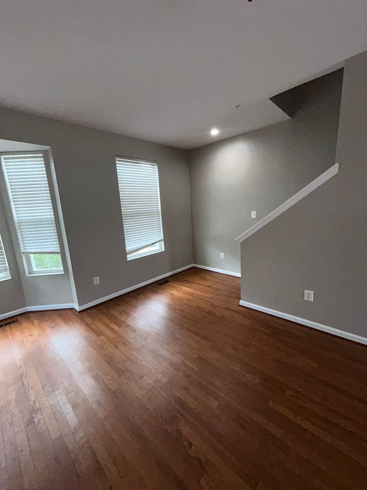 Empty room with hardwood floors, gray walls, and a staircase along the right wall.