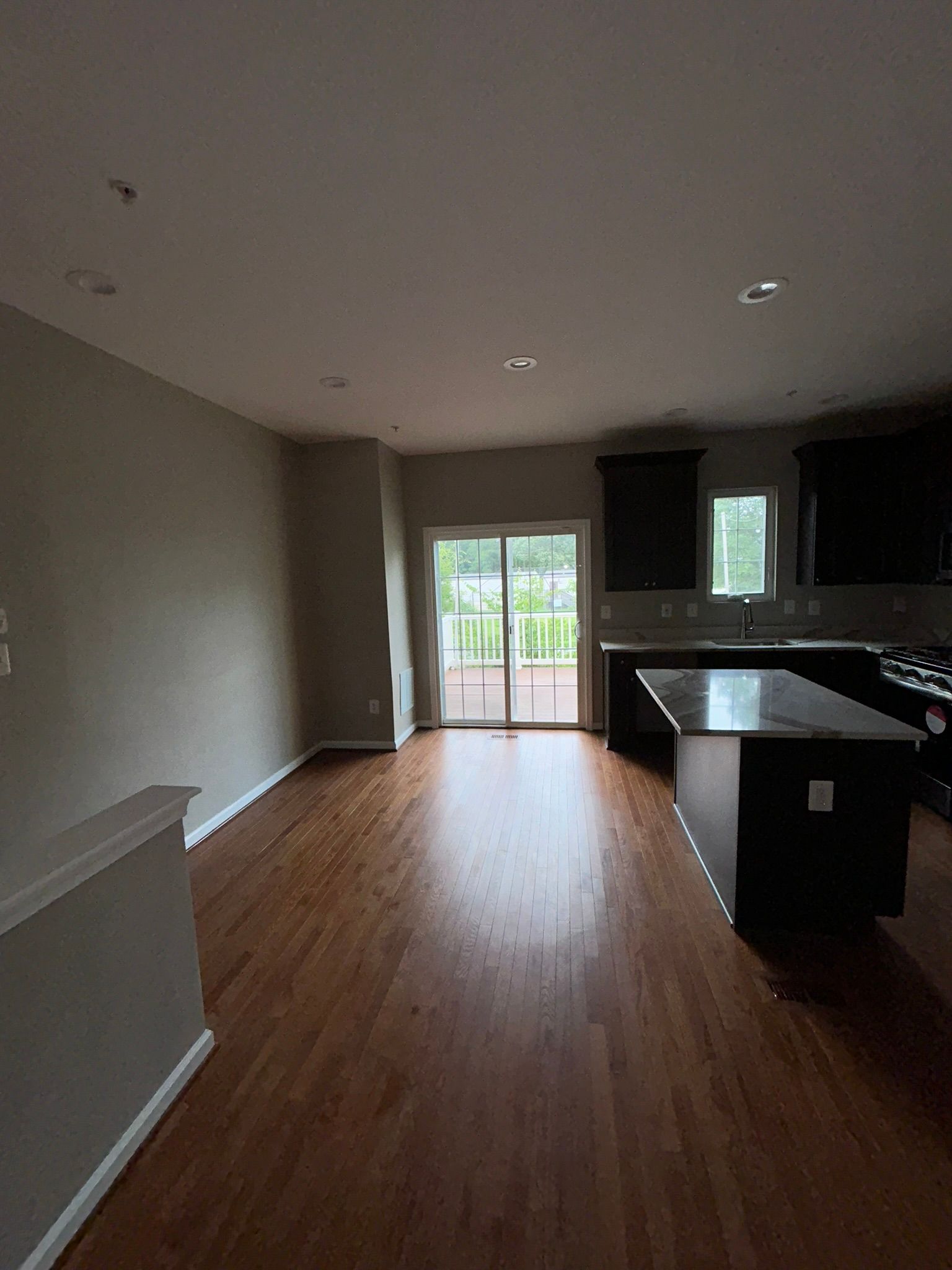 Empty modern kitchen and dining area with hardwood floors, dark cabinets, and glass doors to a patio