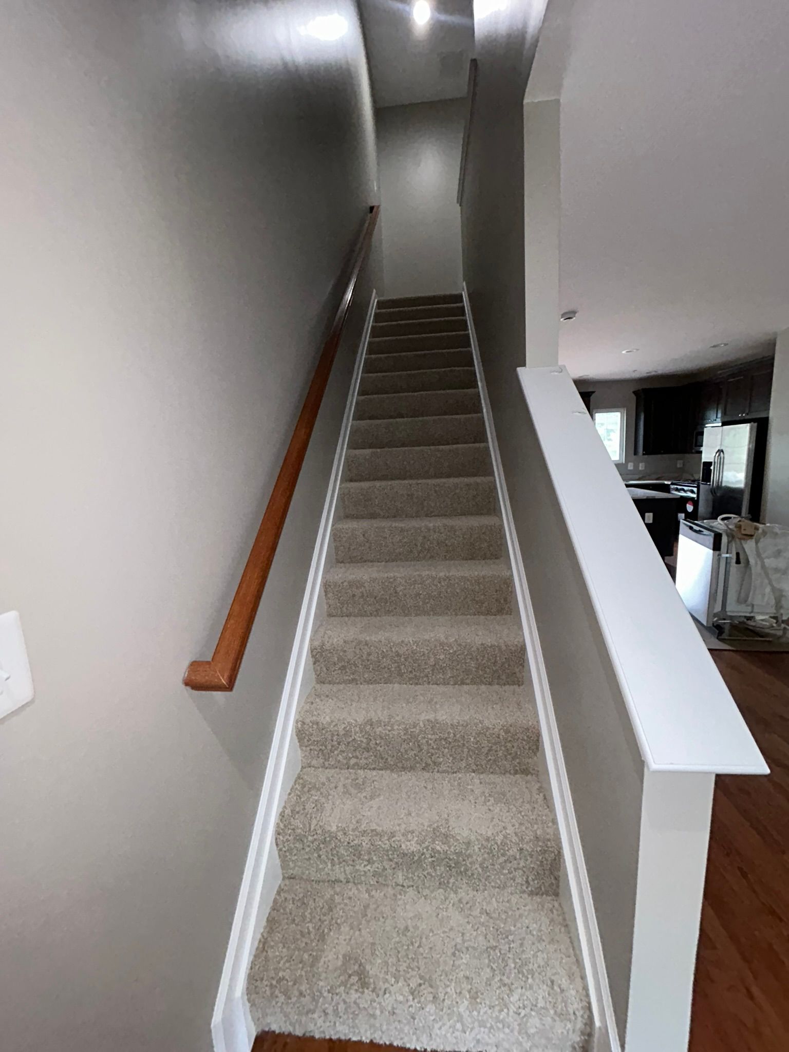 Narrow carpeted staircase with white walls and wooden handrail in a house interior
