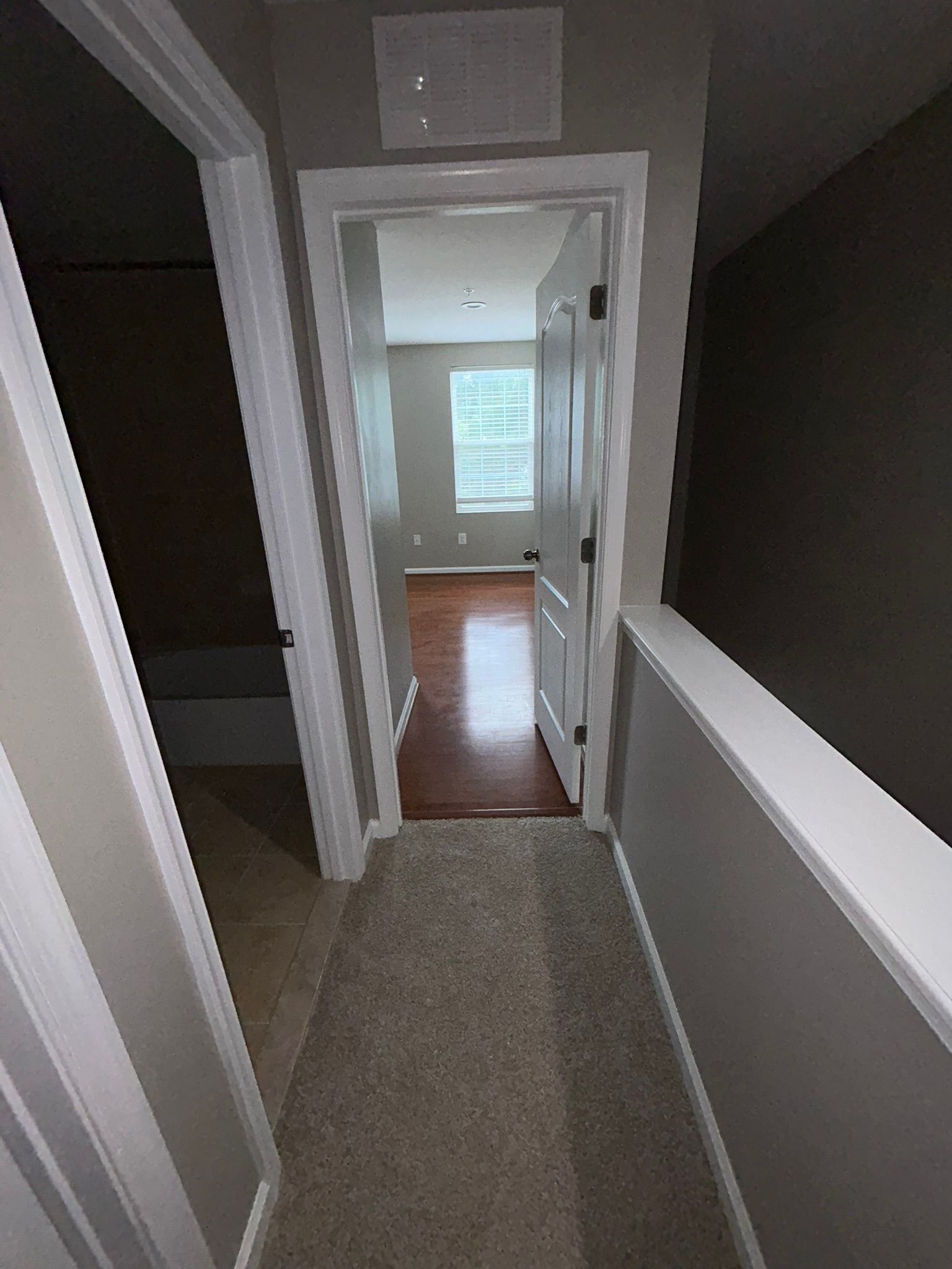 Hallway with carpeted floor, open white doors, and a bright room with a window at the end
