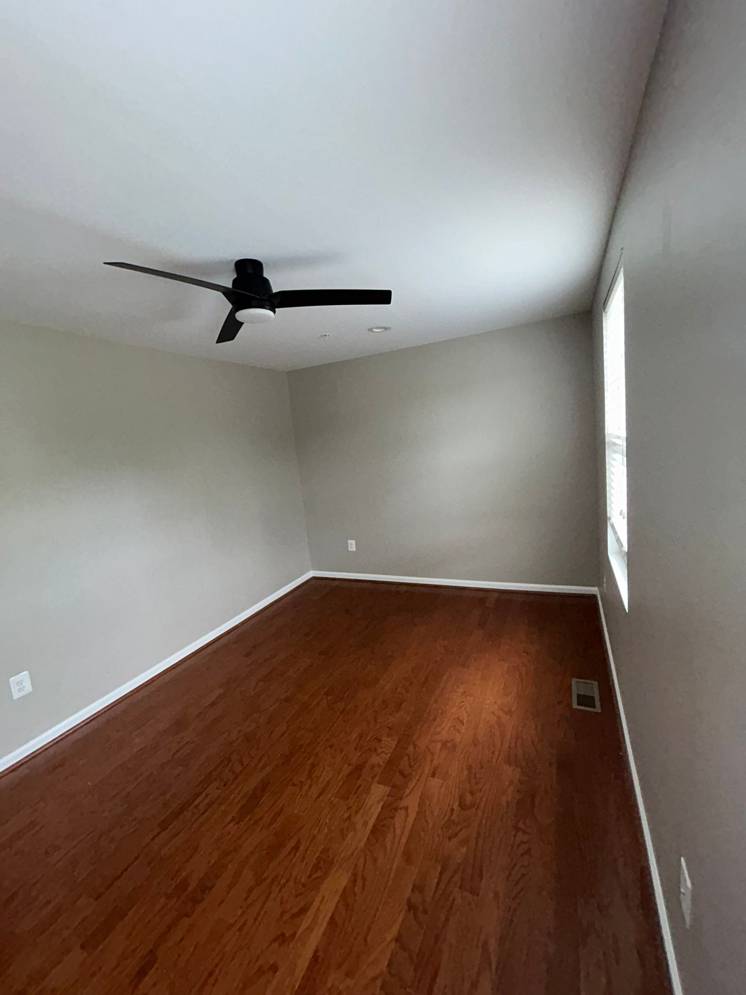 Empty room with hardwood floor, white walls, a ceiling fan, and a window with blinds.