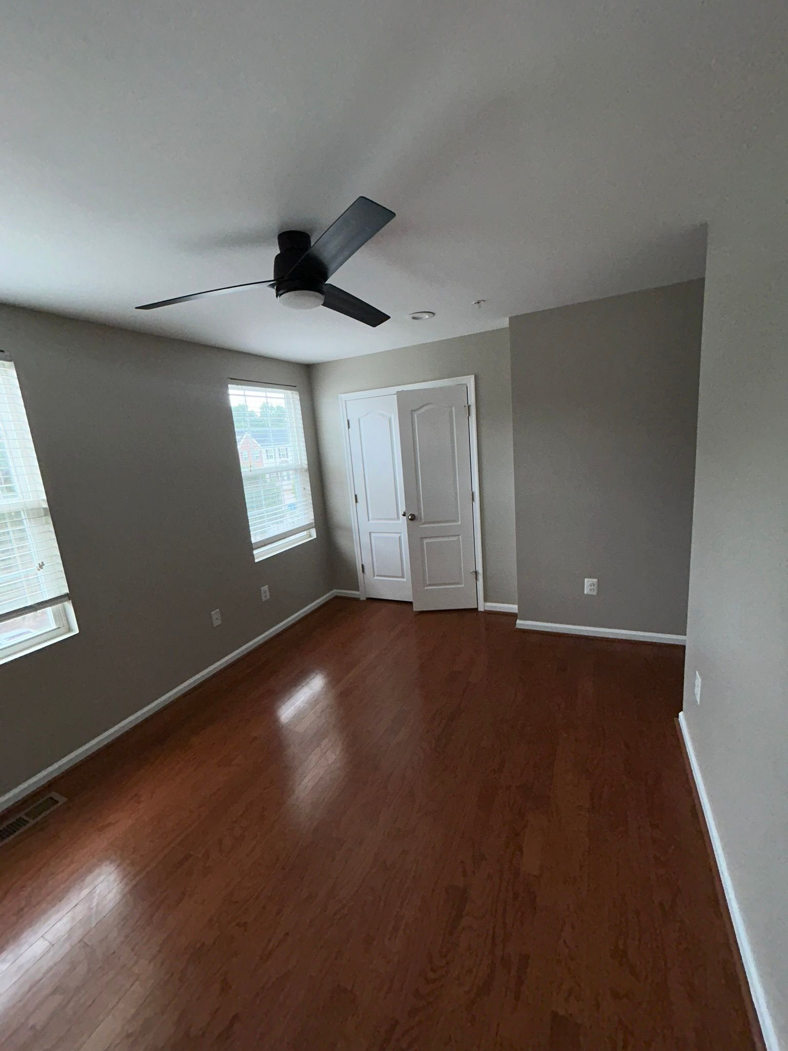 Empty unfurnished room with wood floors, gray walls, windows, and a ceiling fan