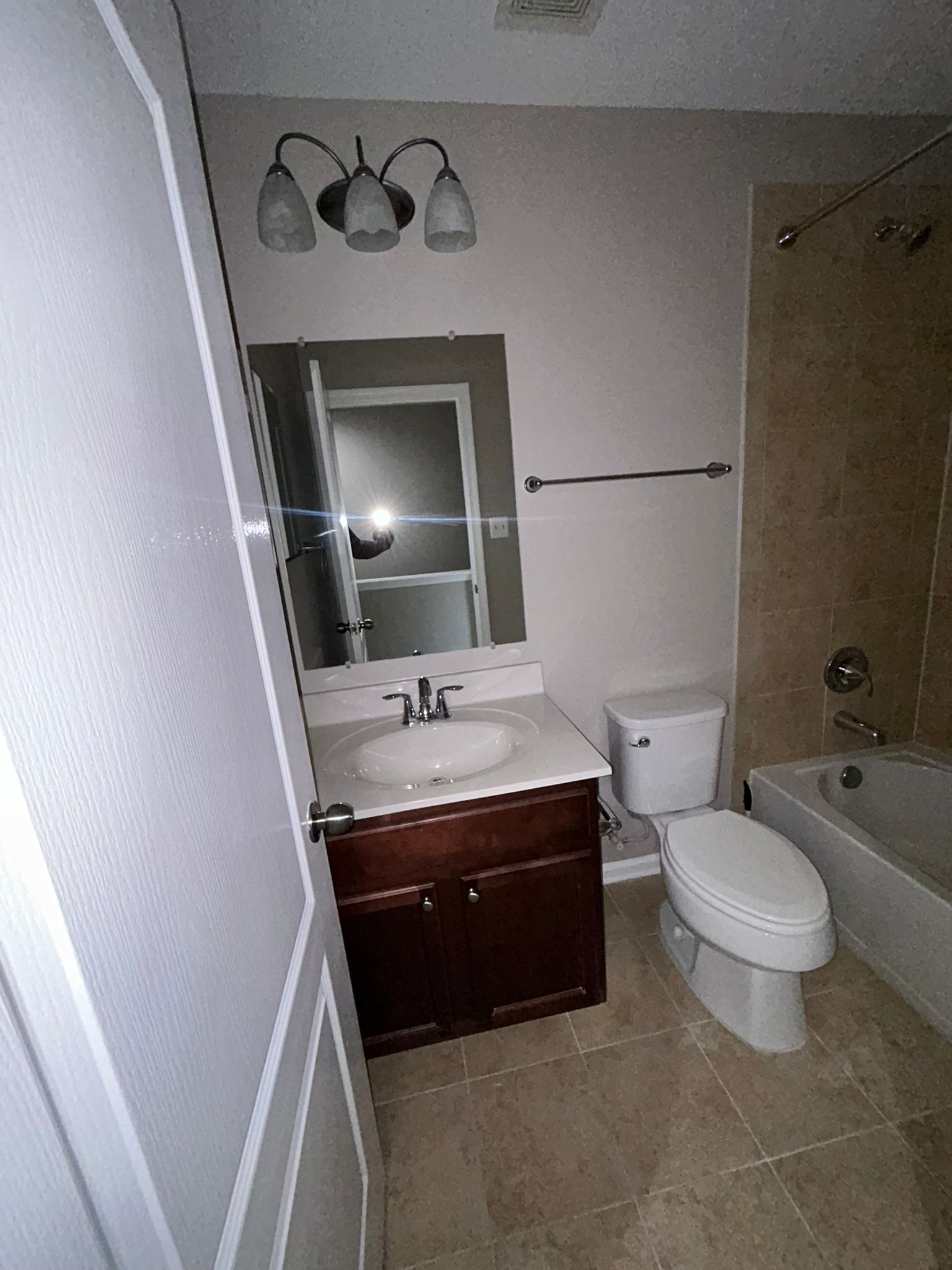 Small bathroom with toilet, sink, vanity, tub, and mirror light.