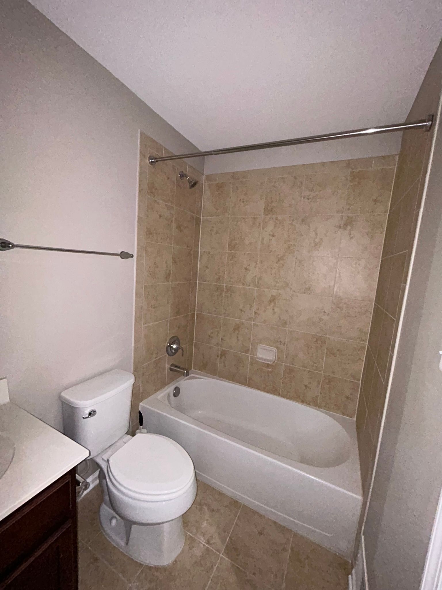 Small beige bathroom with a toilet, bathtub, and brown vanity.