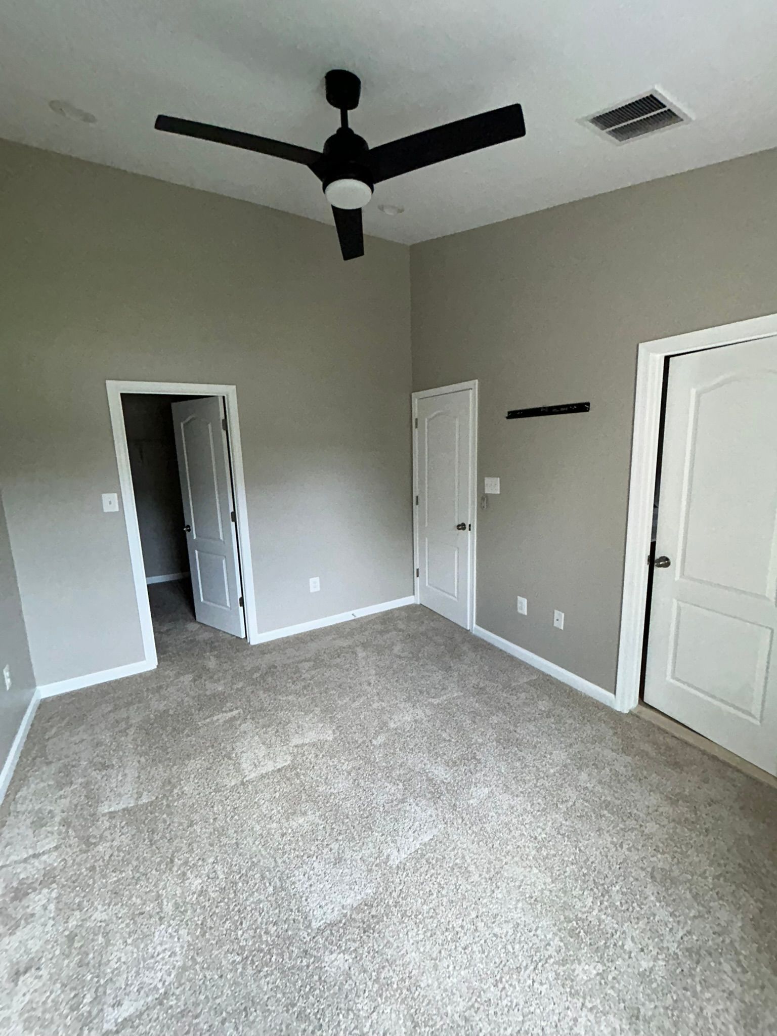 Empty beige bedroom with carpet, ceiling fan, two doorways, and a white door on the right