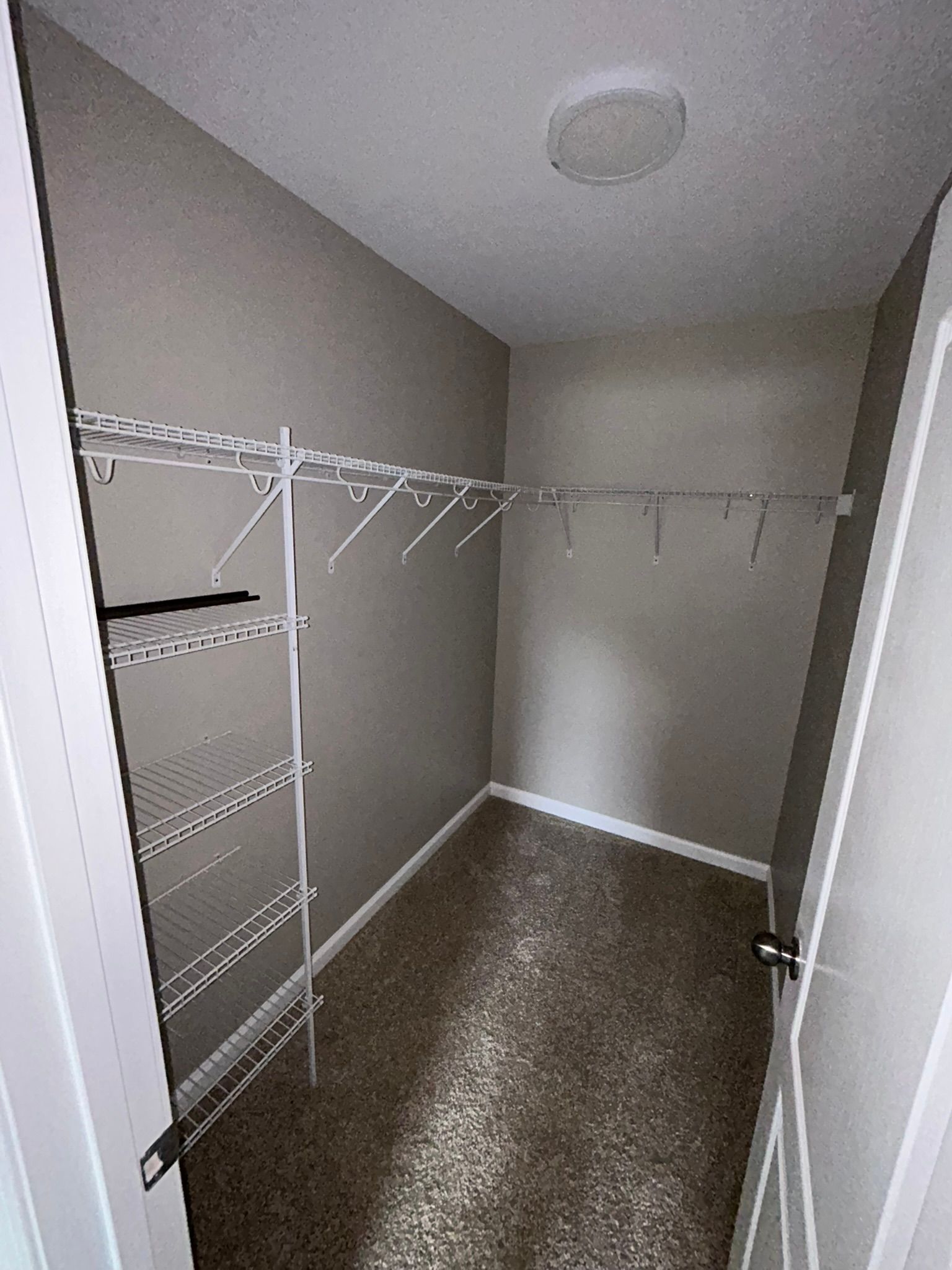 Empty walk-in closet with wire shelving, hanging rods, and beige walls.