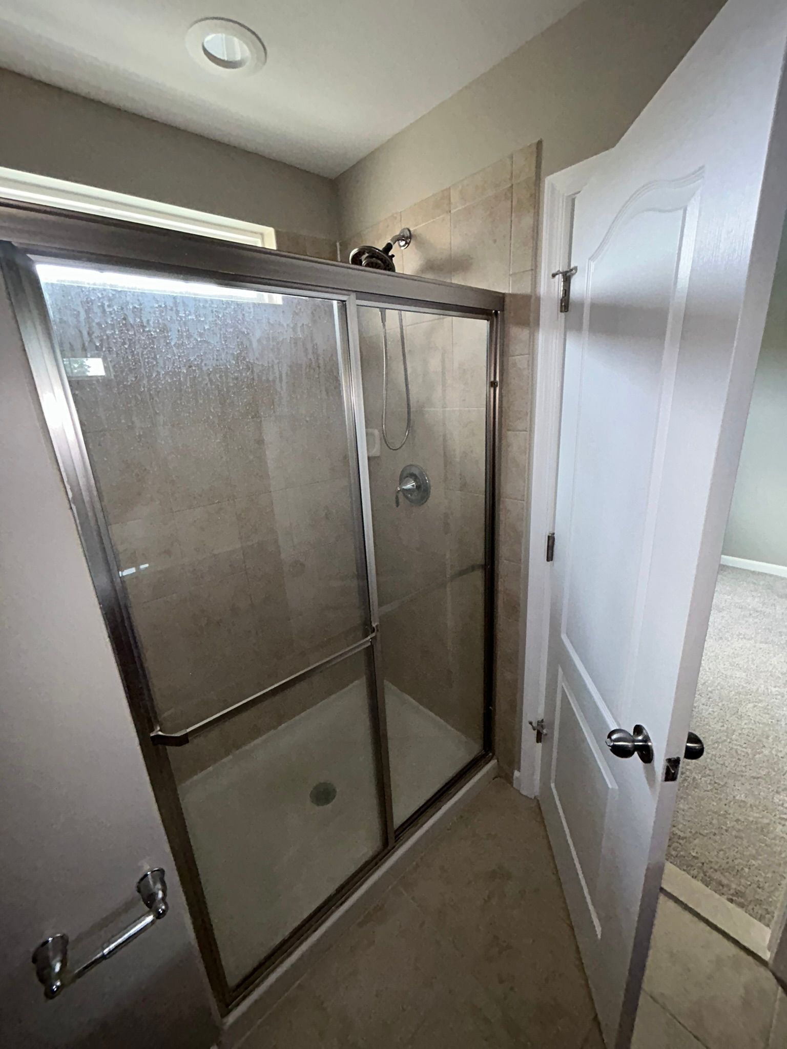 Small bathroom with a glass shower enclosure, beige tile walls, and an open white door