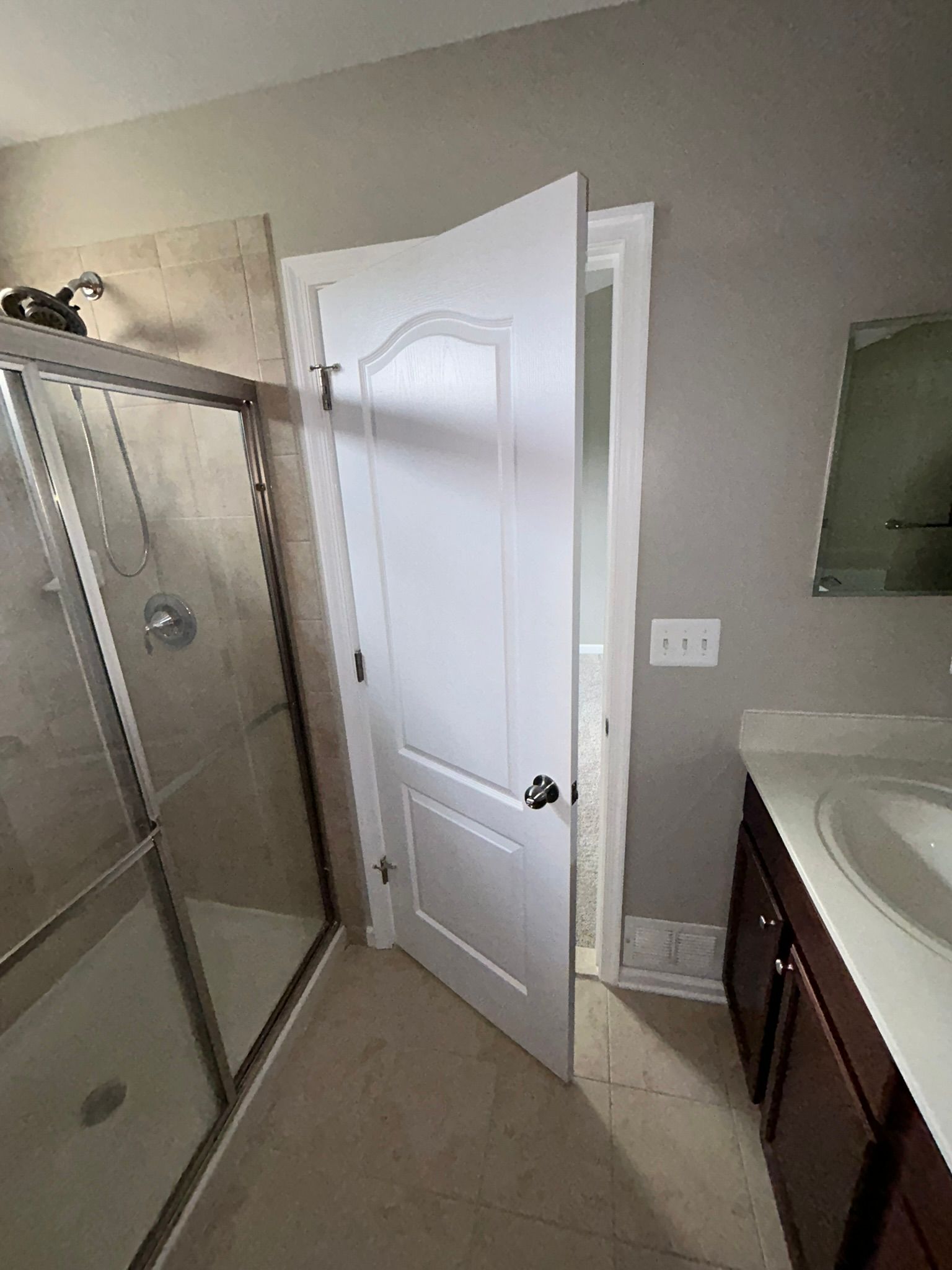 Bathroom with open white door, glass shower enclosure, and vanity sink on the right.