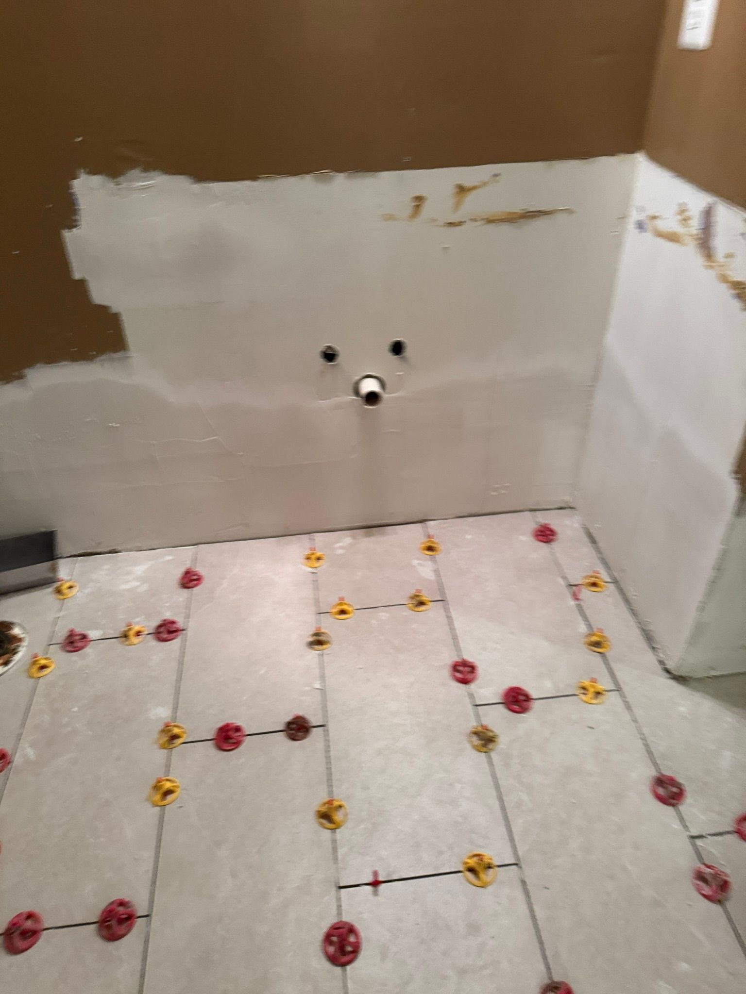 Partially tiled bathroom wall with white patching and floor tiles marked by colorful red and yellow spacers