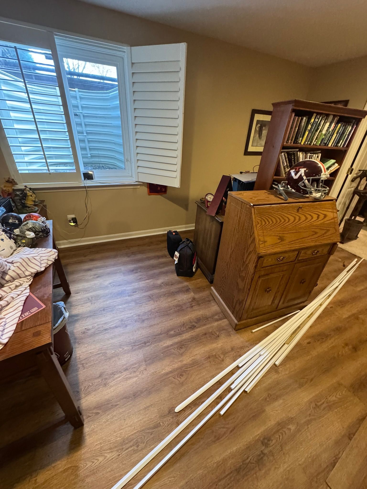 Bedroom with open shuttered window, wooden dresser, and long white rods on the floor.
