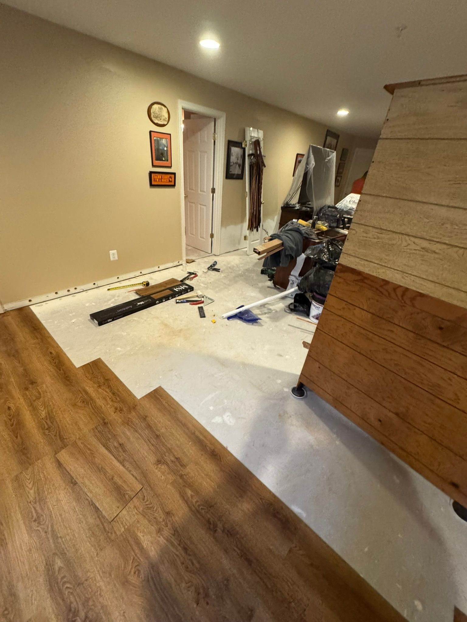 Renovation scene with wood flooring, tools, and debris in a hallway beside a partially finished wall.