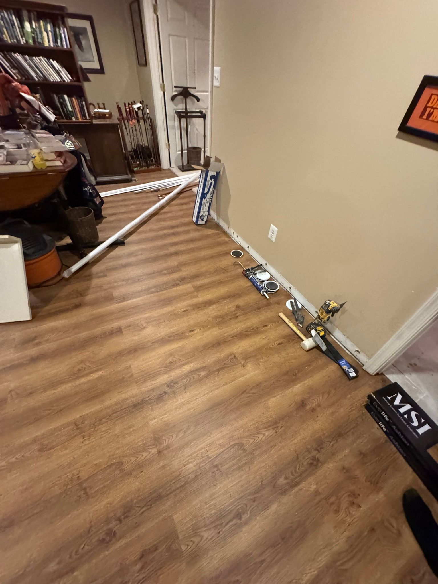 Indoor room with wood floor and white walls, showing scattered tools and a long pole near a work area.
