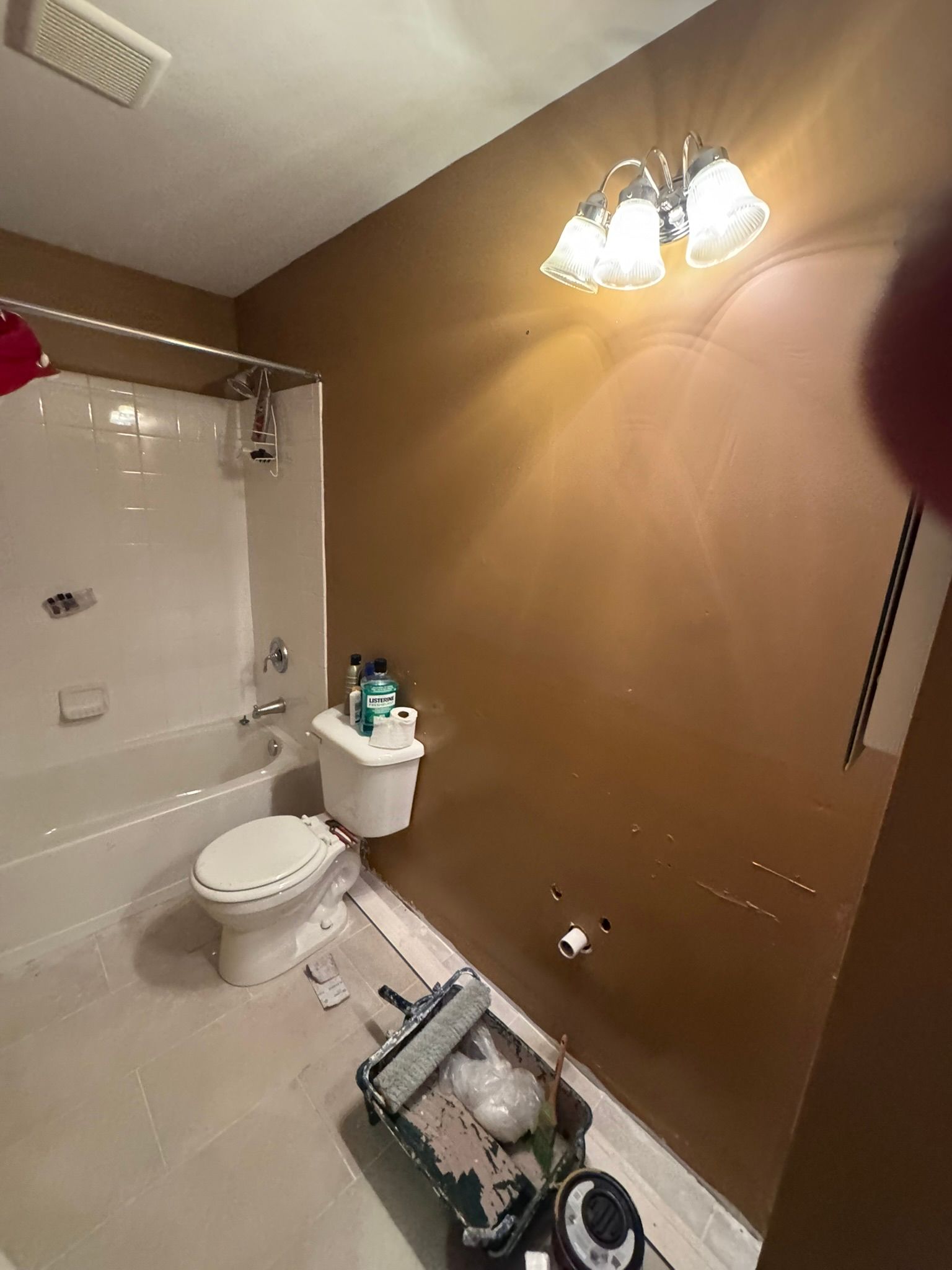 Small bathroom under renovation with tub, toilet, sink, tan walls, and tools on the floor