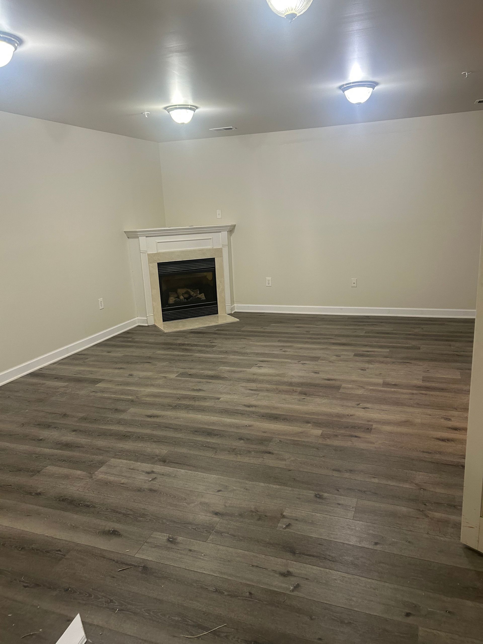 Empty living room with gray wood floors, white walls, and a small fireplace.