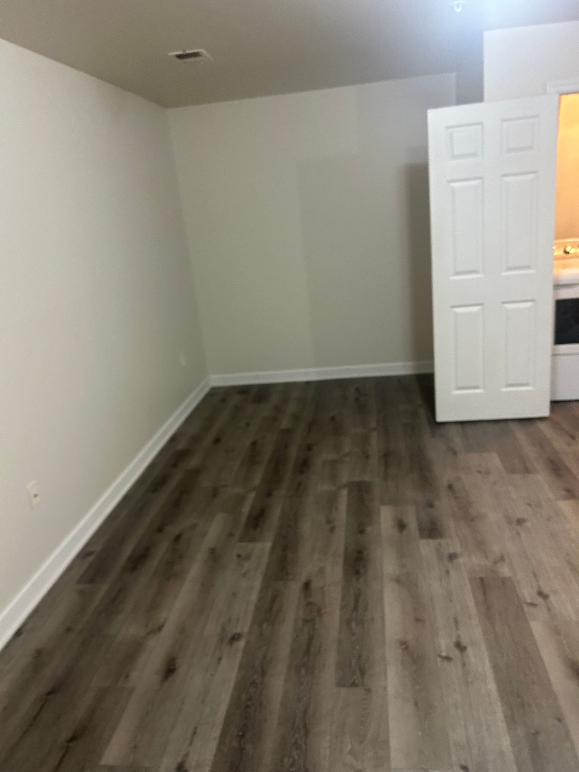 Empty room with gray wood flooring, white walls, and an open door on the right.