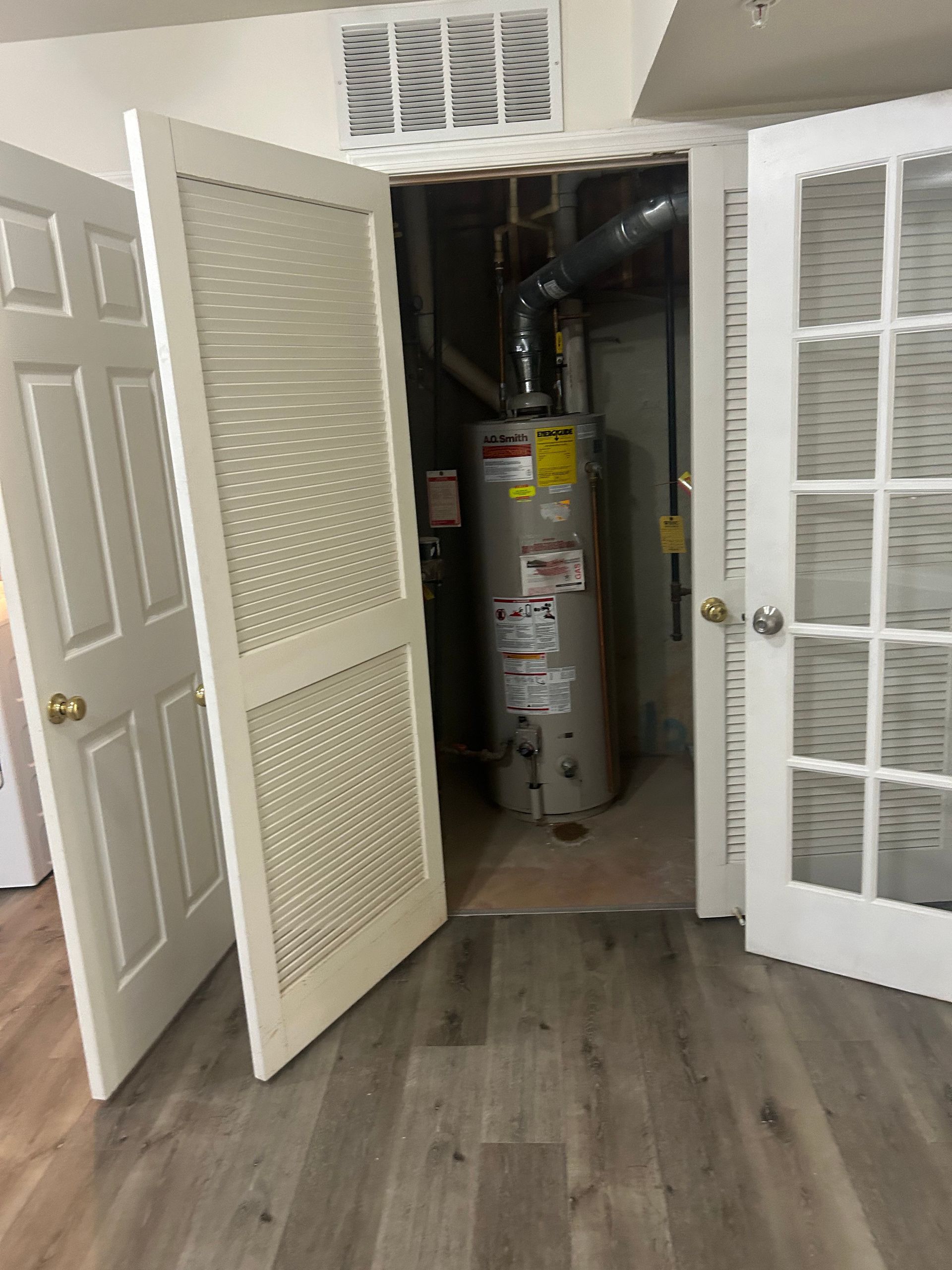 Open closet with a water heater and furnace in a hallway, doors open on both sides.