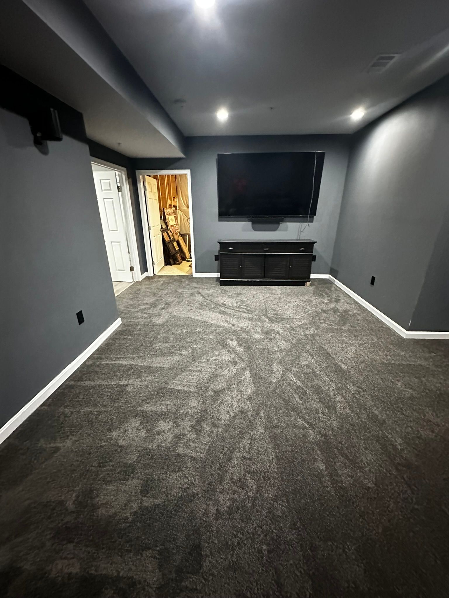 Empty gray media room with dark carpet, recessed lights, TV, and console cabinet on the far wall