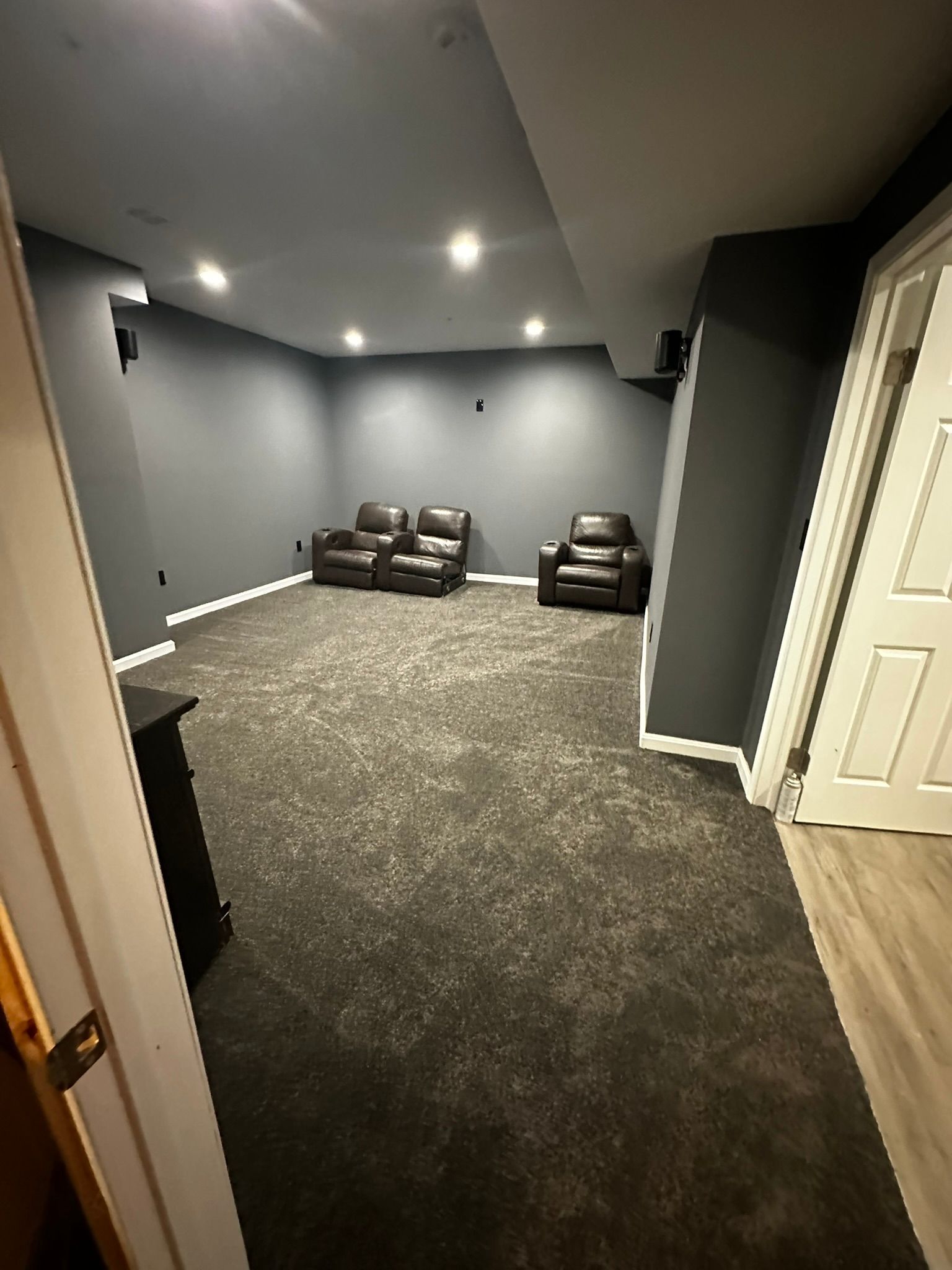 Gray carpeted media room with two brown recliners and recessed ceiling lights