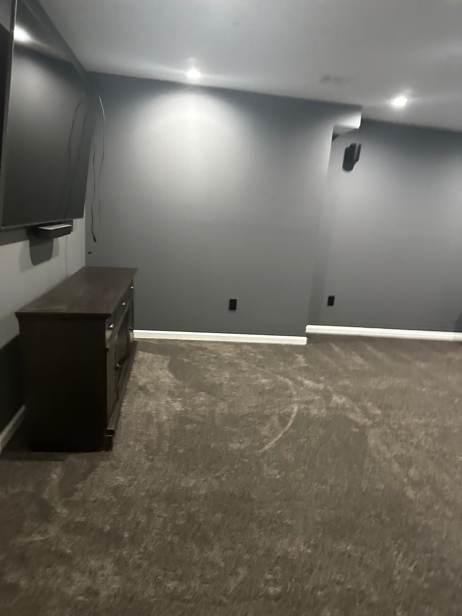 Empty gray room with carpet, recessed lights, wall-mounted TV, and a dark dresser against the left wall