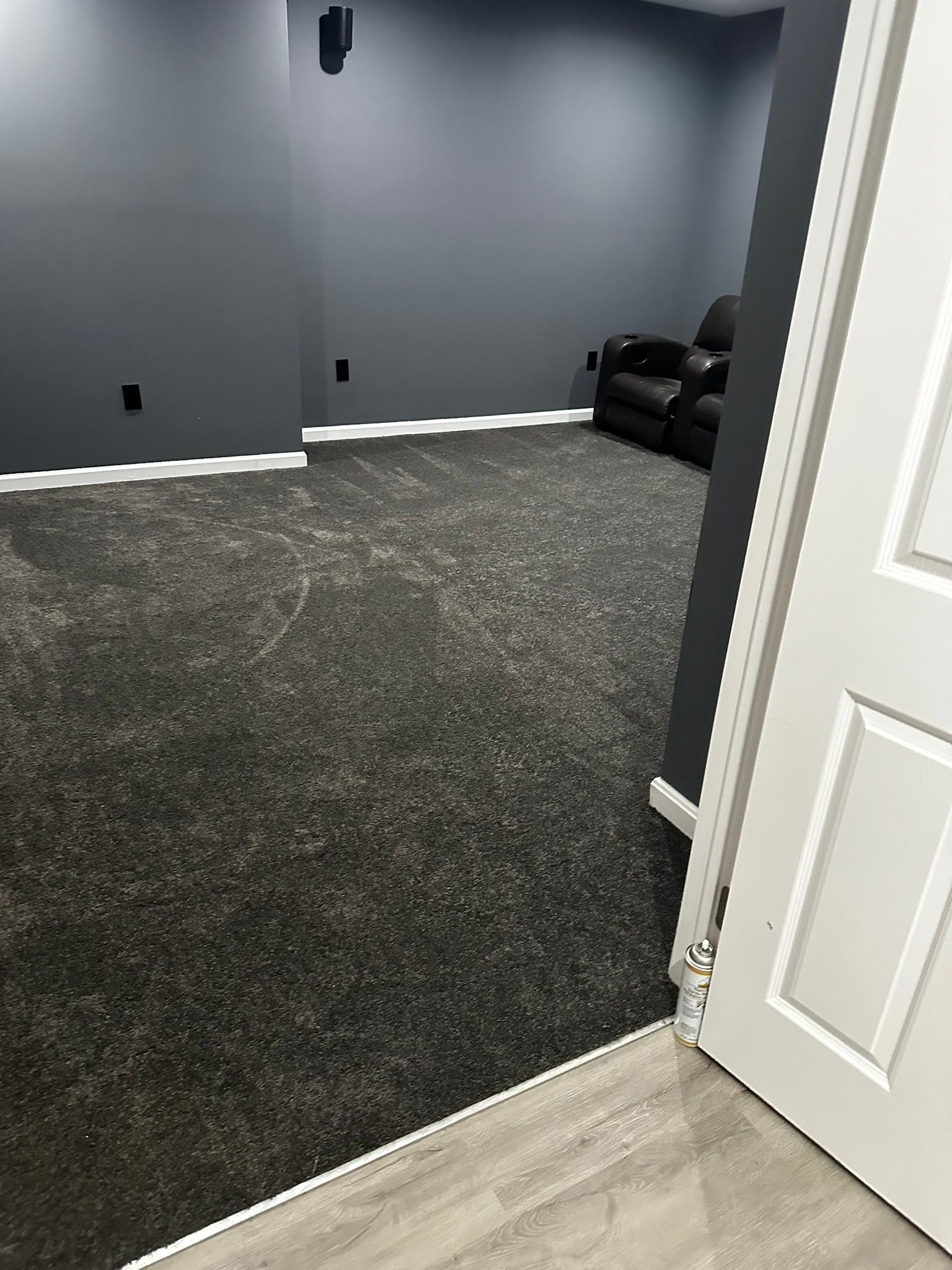 Open door to a carpeted room with gray walls and a black couch in the corner.