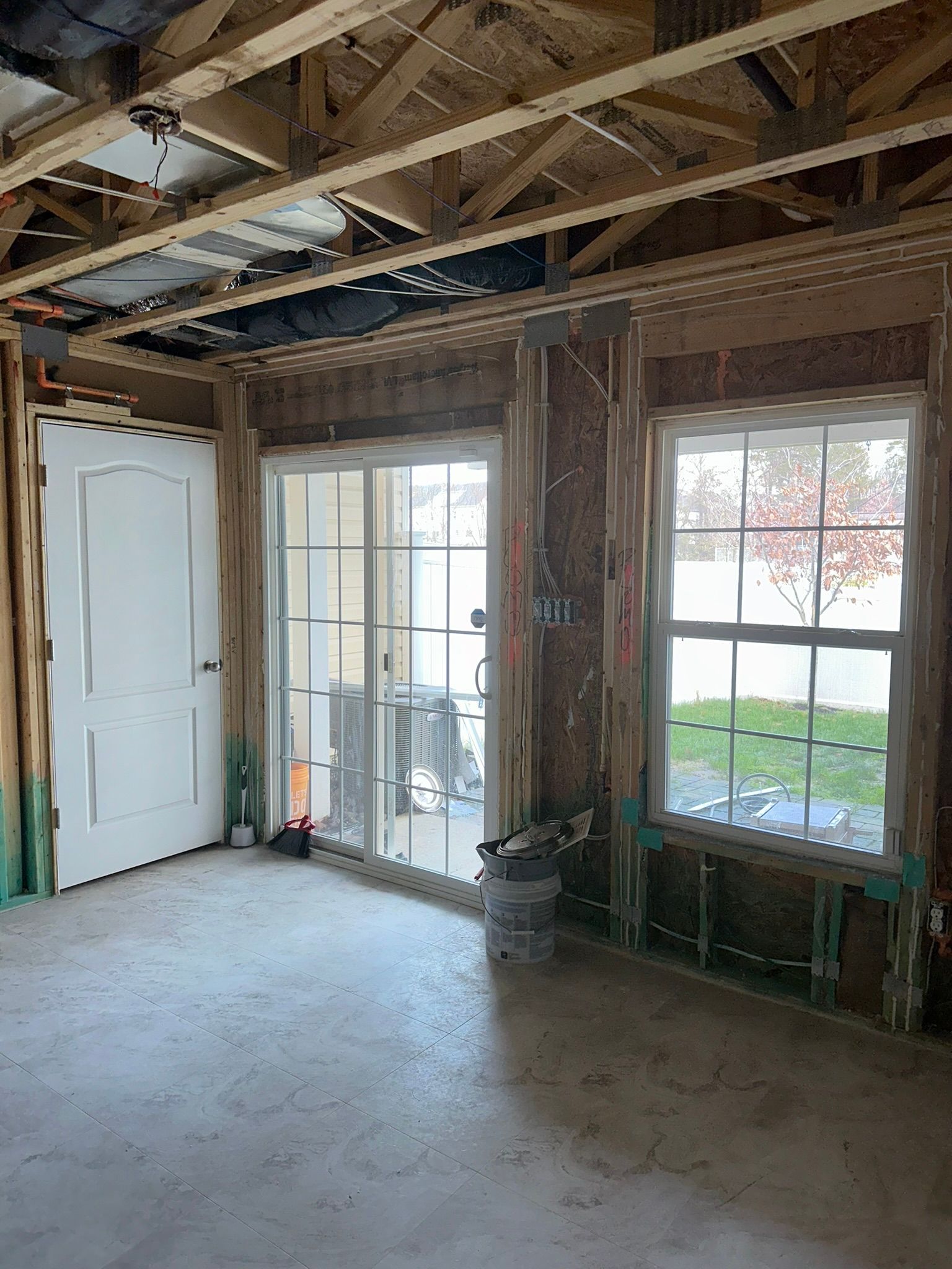 Interior of an unfinished room with exposed beams, bare drywall, large windows, and a concrete floor