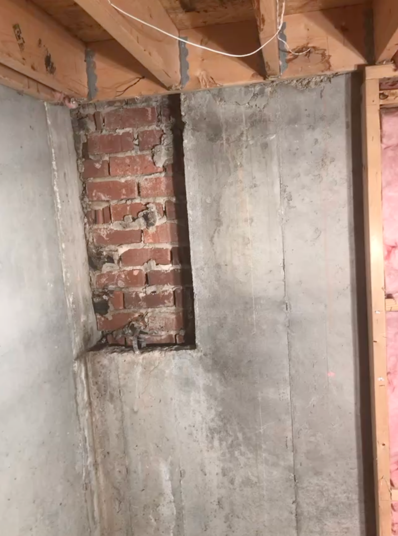 Partially finished interior wall with exposed brick, gray plaster, and open ceiling beams