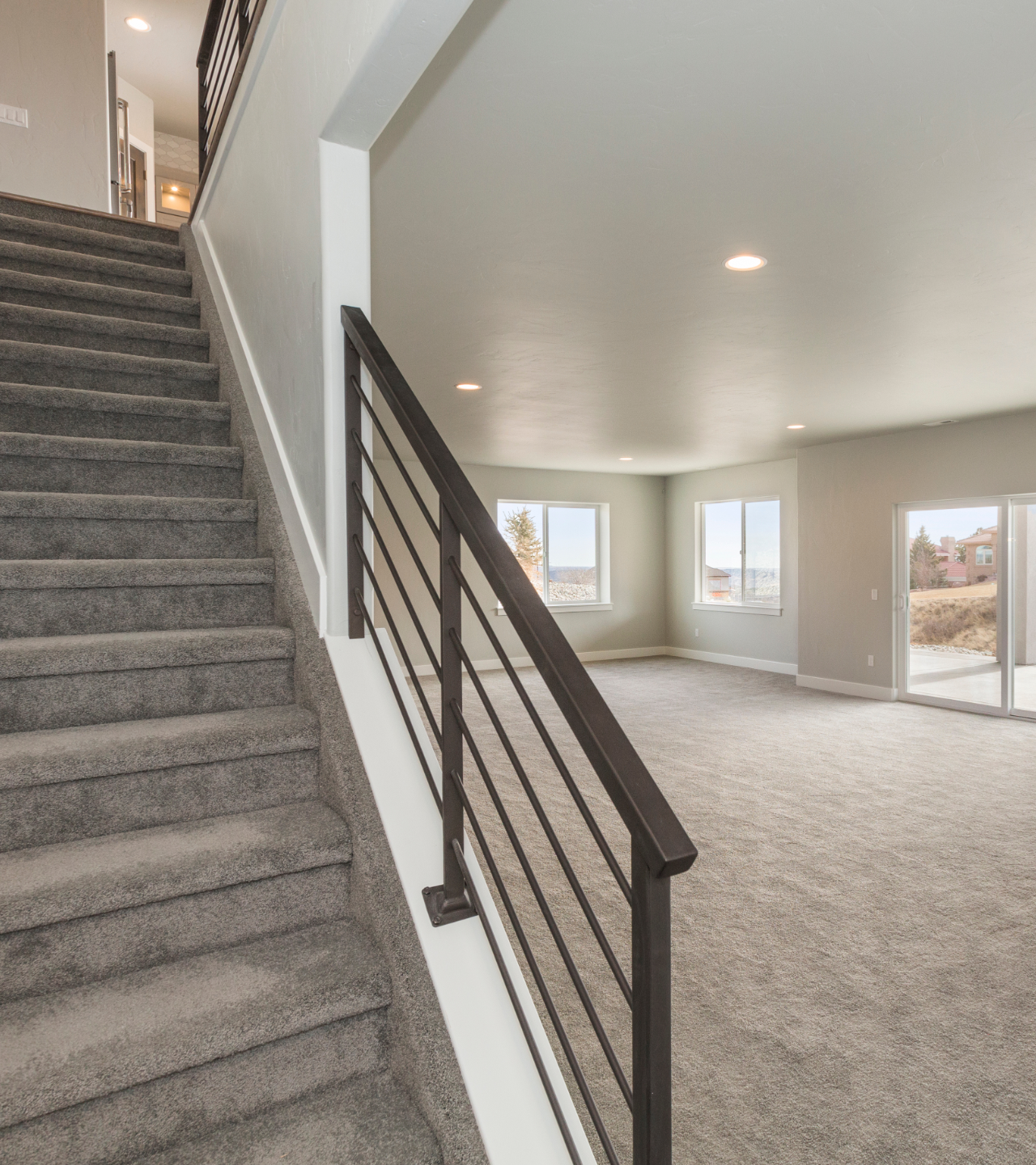 Carpeted staircase beside an open living room with white walls, gray railings, and bright windows
