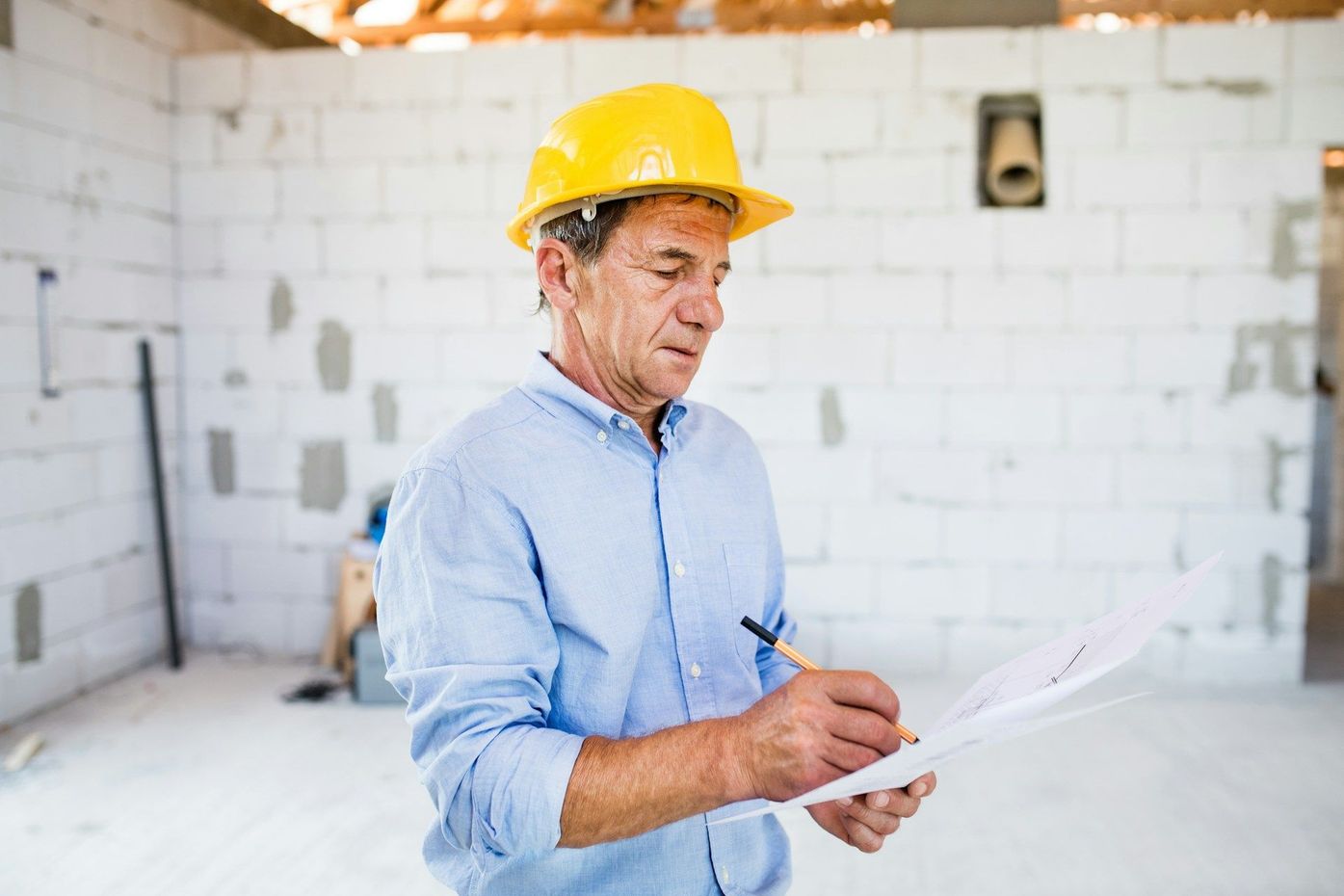 Construction worker in a yellow hard hat reviewing plans inside a renovation site