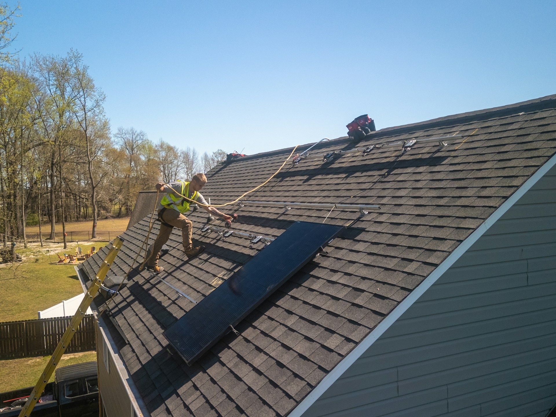 Worker on a shingled roof installing solar panels on a sunny day