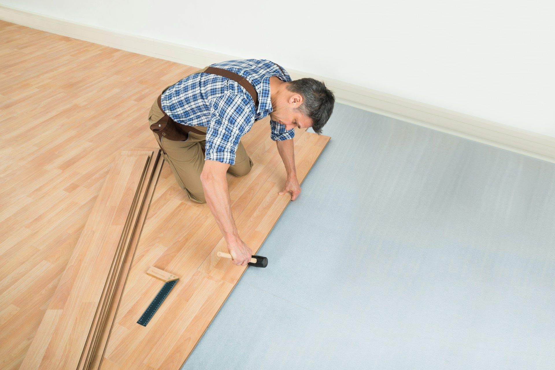 Worker installing wood flooring with a seam roller beside unfinished planks and blue underlayment