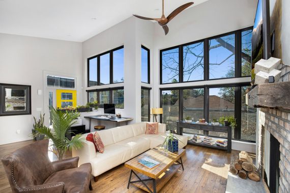 Living room with tall windows, leather chair, beige sofa, and fireplace.