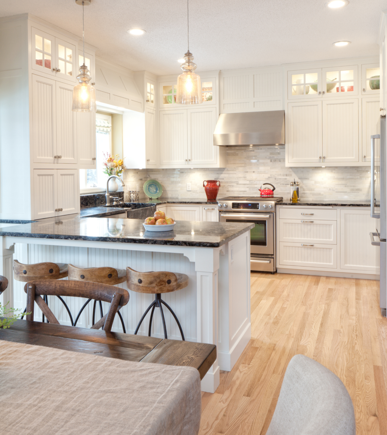 Bright white modern kitchen with island, wood floors, pendant lights, and stainless steel range.