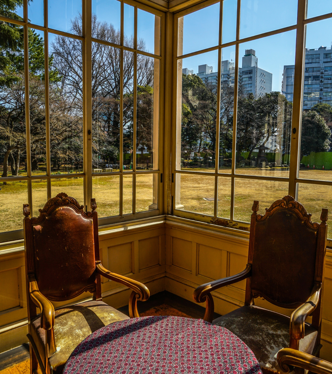 Sunlit corner with two ornate chairs and a round table overlooking a park and city skyline