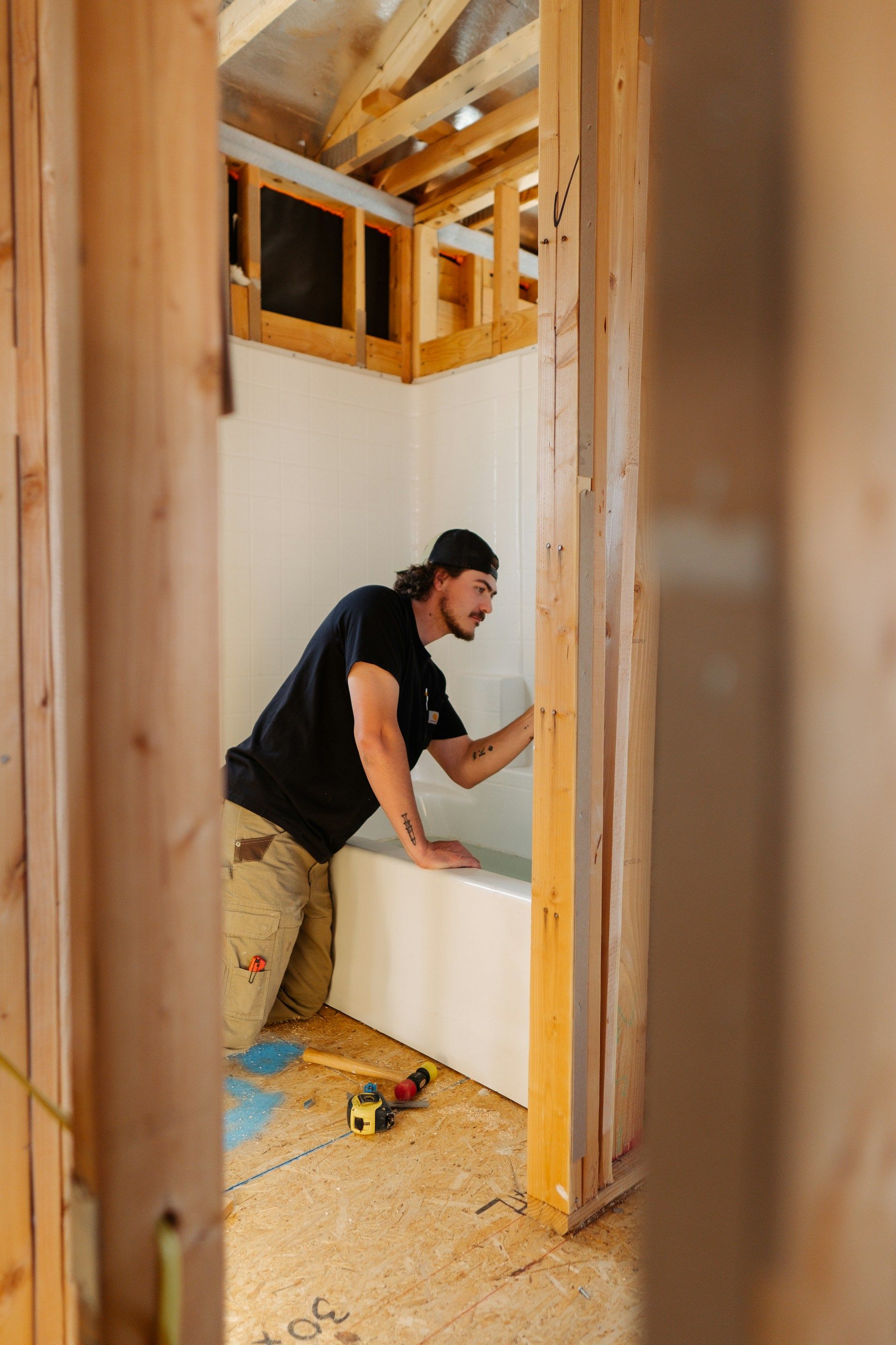 Person installing a white wall panel inside a framed room with exposed wood studs and tools on the floor