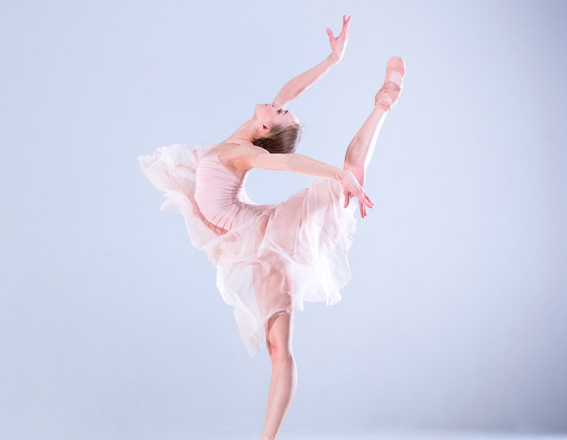 A ballerina is standing on one leg in a pink tutu.