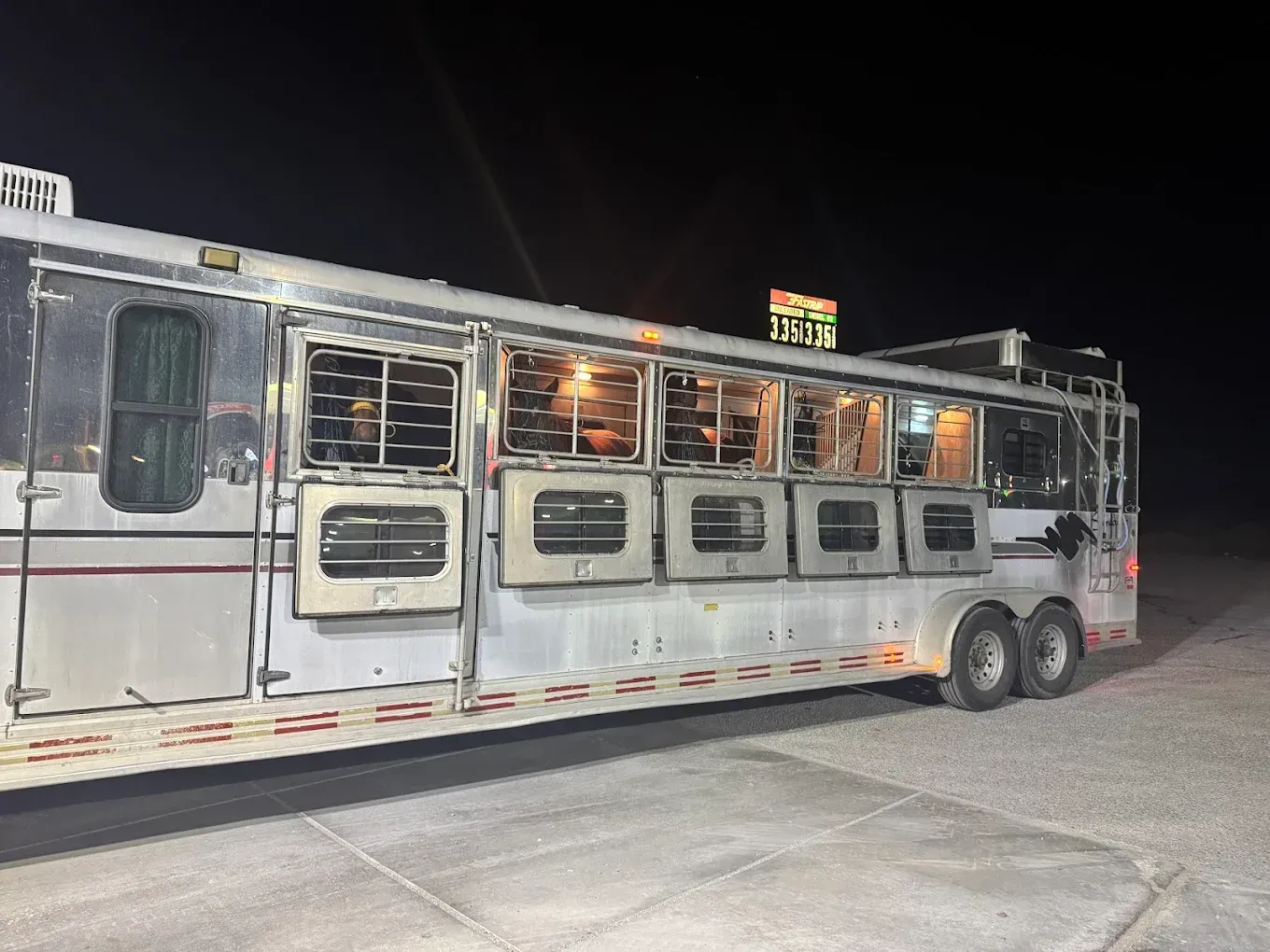 A horse trailer is parked in a parking lot at night.