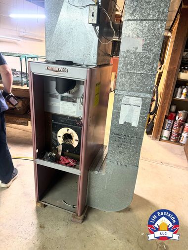 Open metal cabinet beside a gray pillar in a dim indoor hallway, with bottles on a shelf in the background.