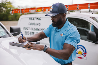 Worker in blue shirt installing a device on a white service truck with a ladder on top